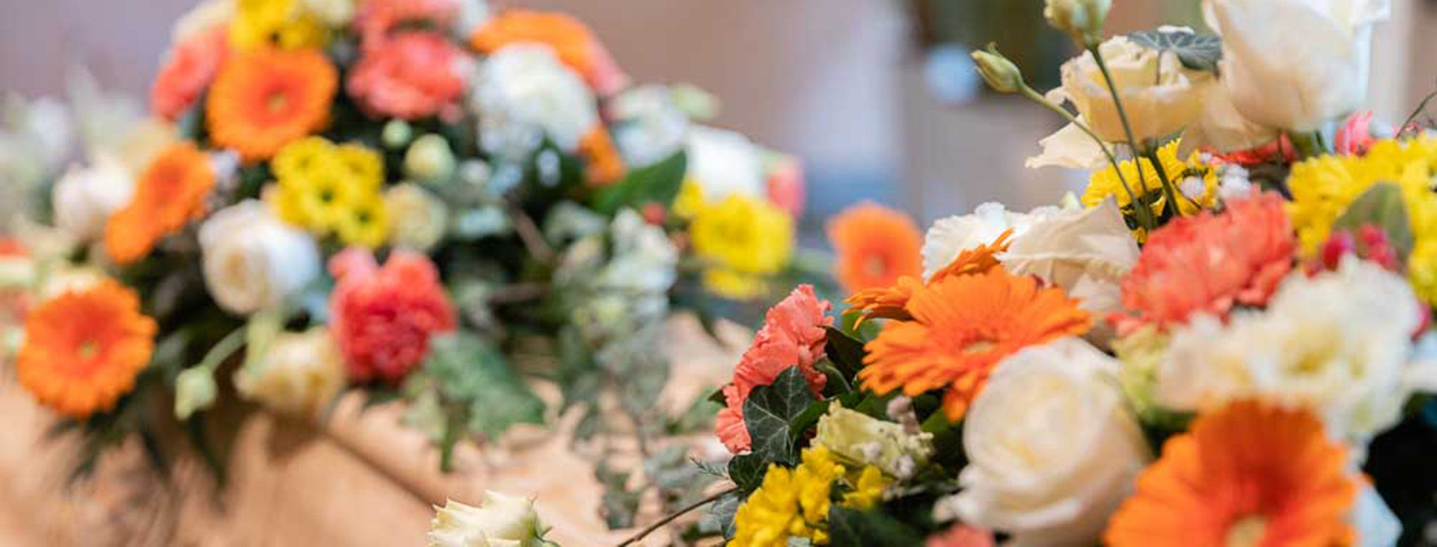 Ein Sarg mit einer liebevoll arrangierten Blumenauflage aus bunten Blüten, die eine warme und feierliche Atmosphäre für die Trauerfeier vermitteln.